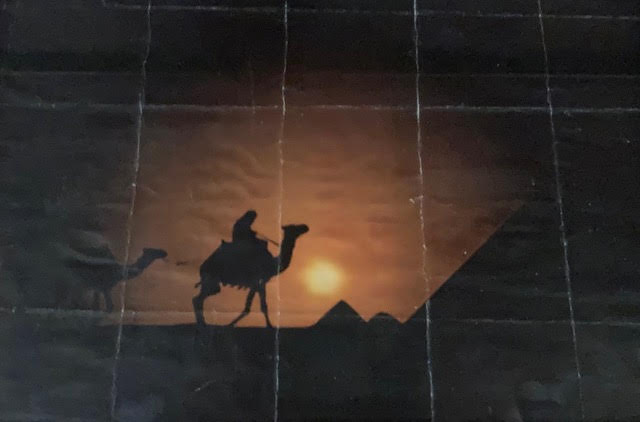 A silhouetted rider on a camel crossing the desert at dusk, pyramids in the distance
